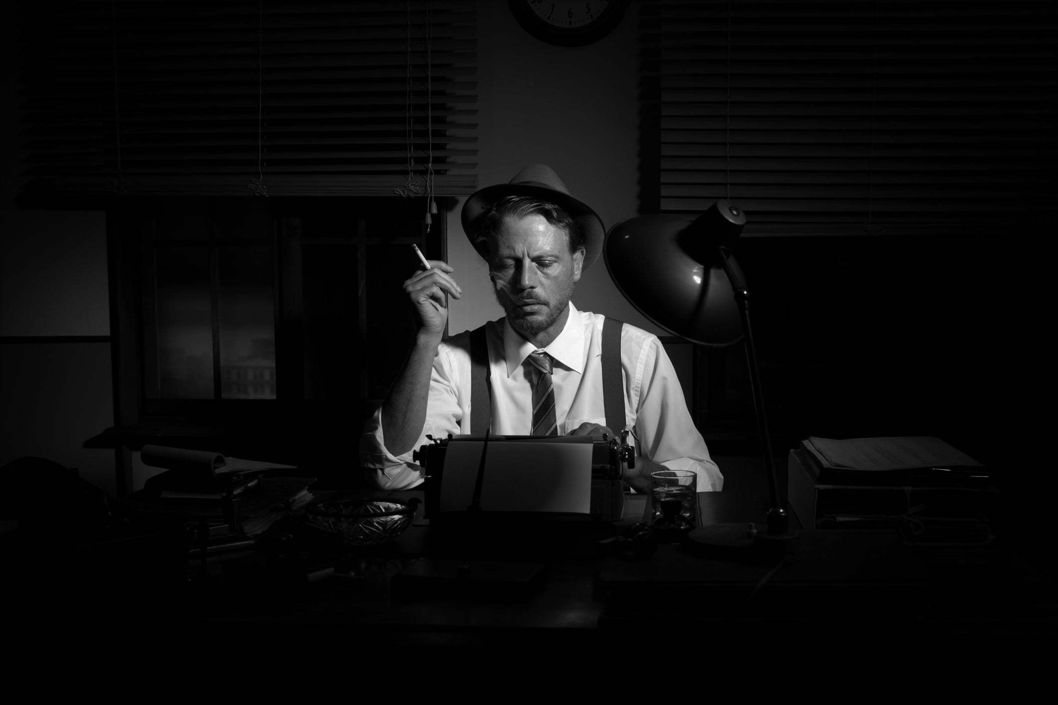 Retro reporter working late typing on a typewriter and smoking a cigarette.